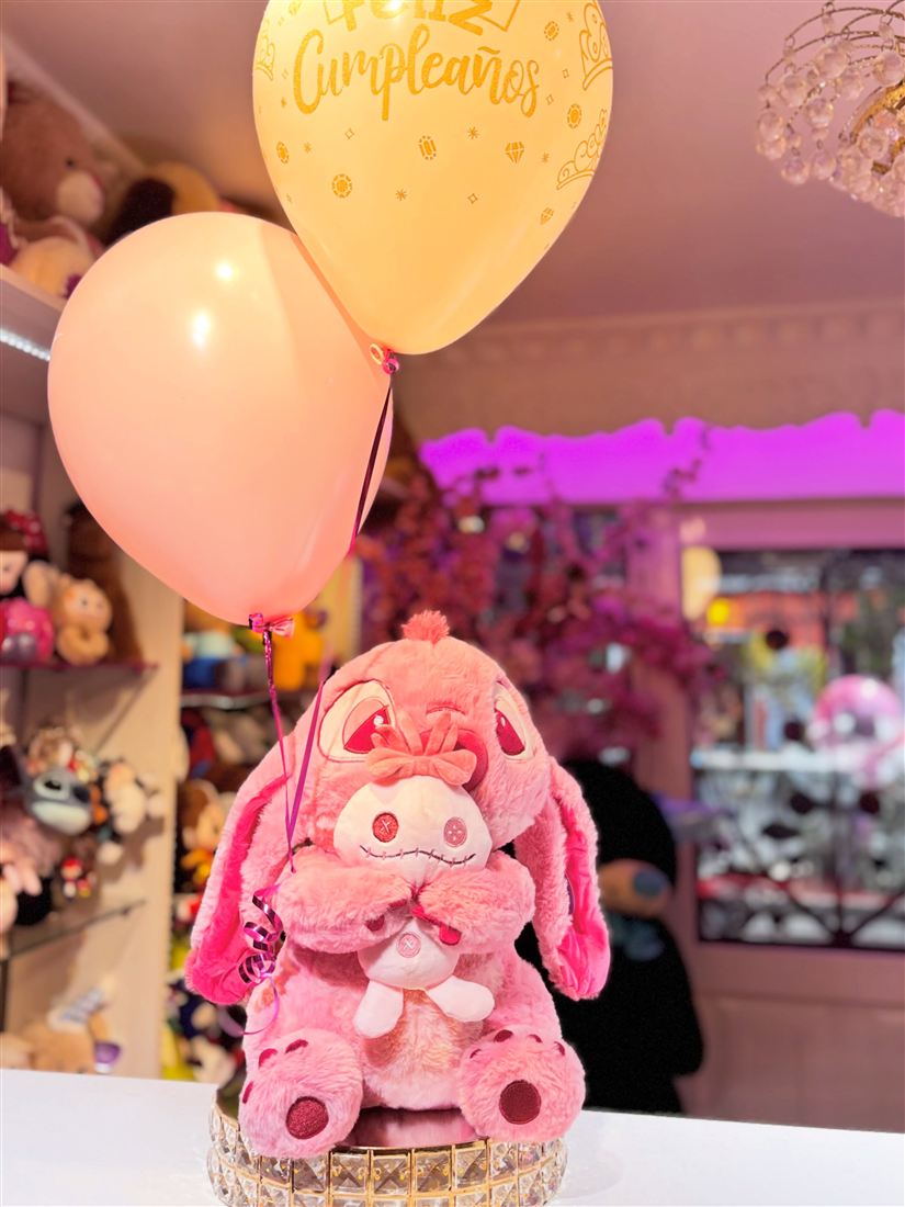 Peluche rosado abrazando otro peluche, con globos en tonos pastel